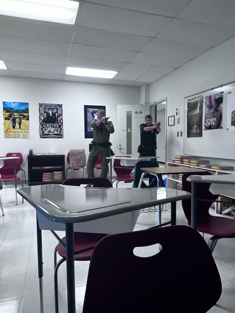 Men in police uniforms hold guns in a classroom.