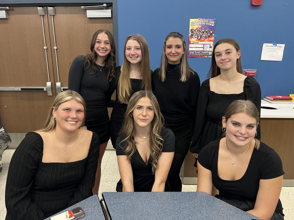 A group of teenagers wearing black smile together at a high school cafeteria table.