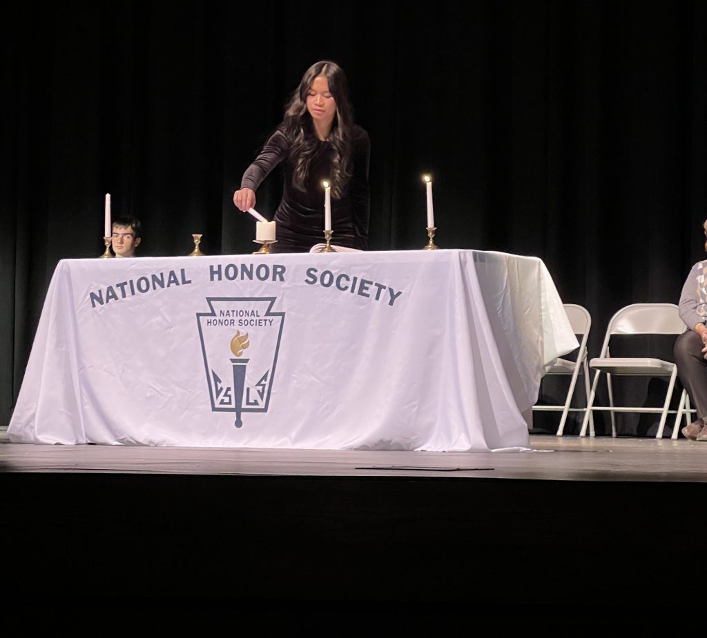 A teenager lights a National Honor Society candle on a stage.