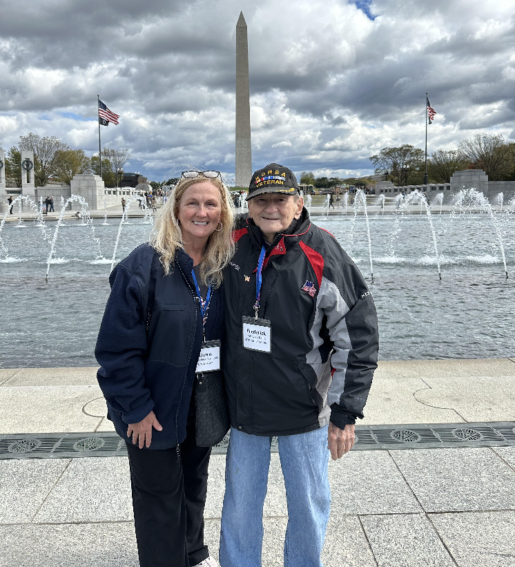 An image of a woman and a U.S. Navy Korean War veteran standing in front of the National Monument and a fountain. 