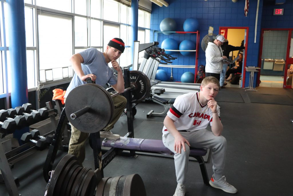Two high school seniors pose next to a bench press in the weight room at Goshen High School.