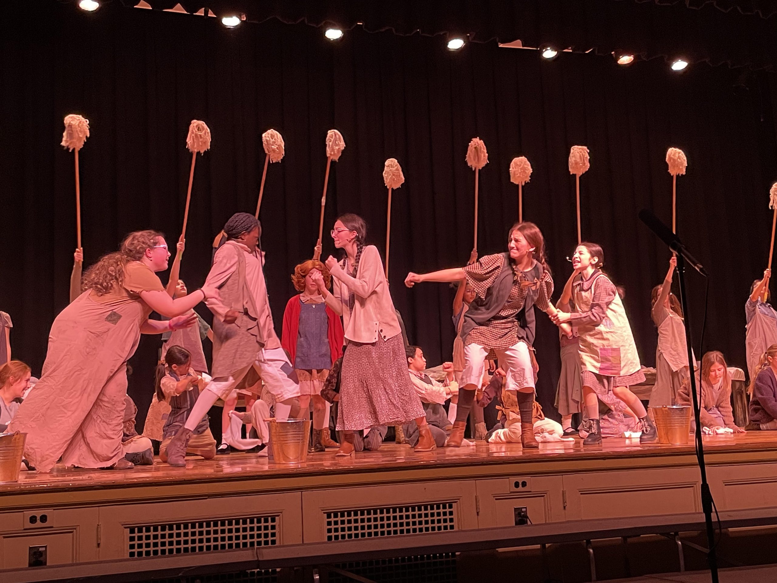The middle school students playing the orphans in the Annie Jr. musical dance together with mops and buckets.