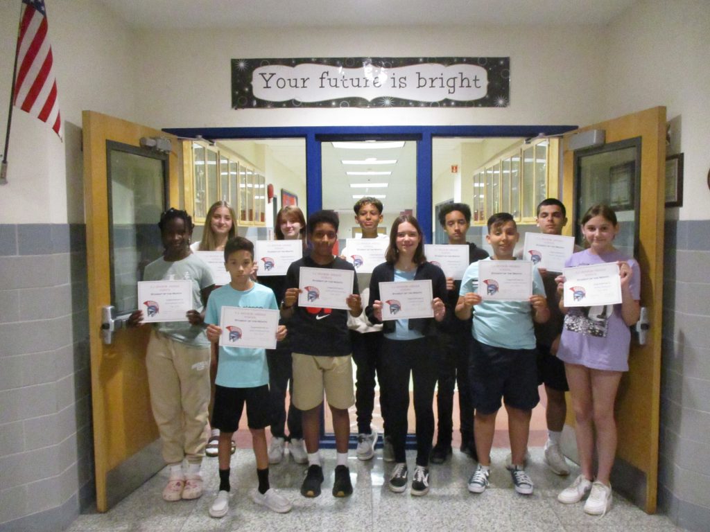 Middle school students smiling holding up certificates in a hallway under a sign that says "Your future is bright."