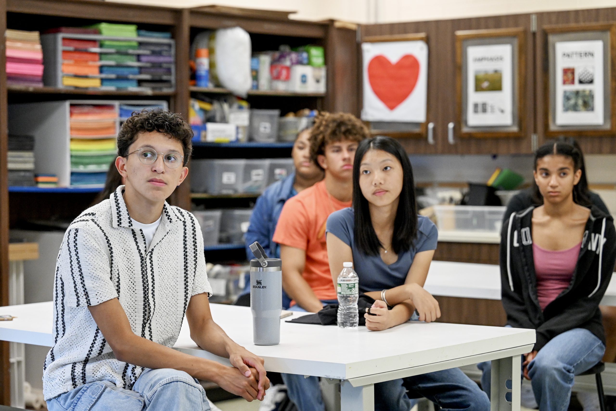 High school students sit at a table in an art classroom