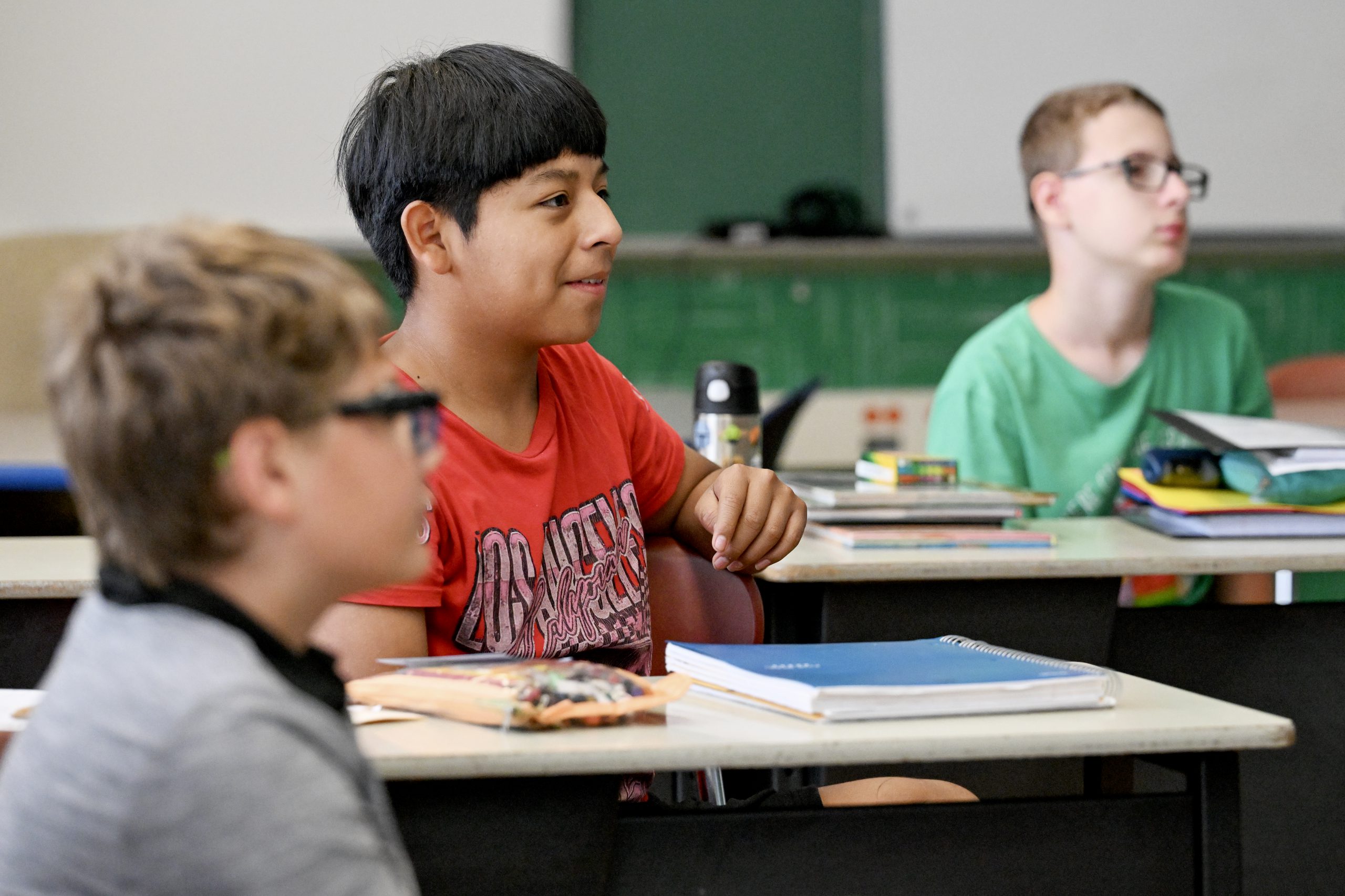 Young teens sit at desks listening to their teacher.