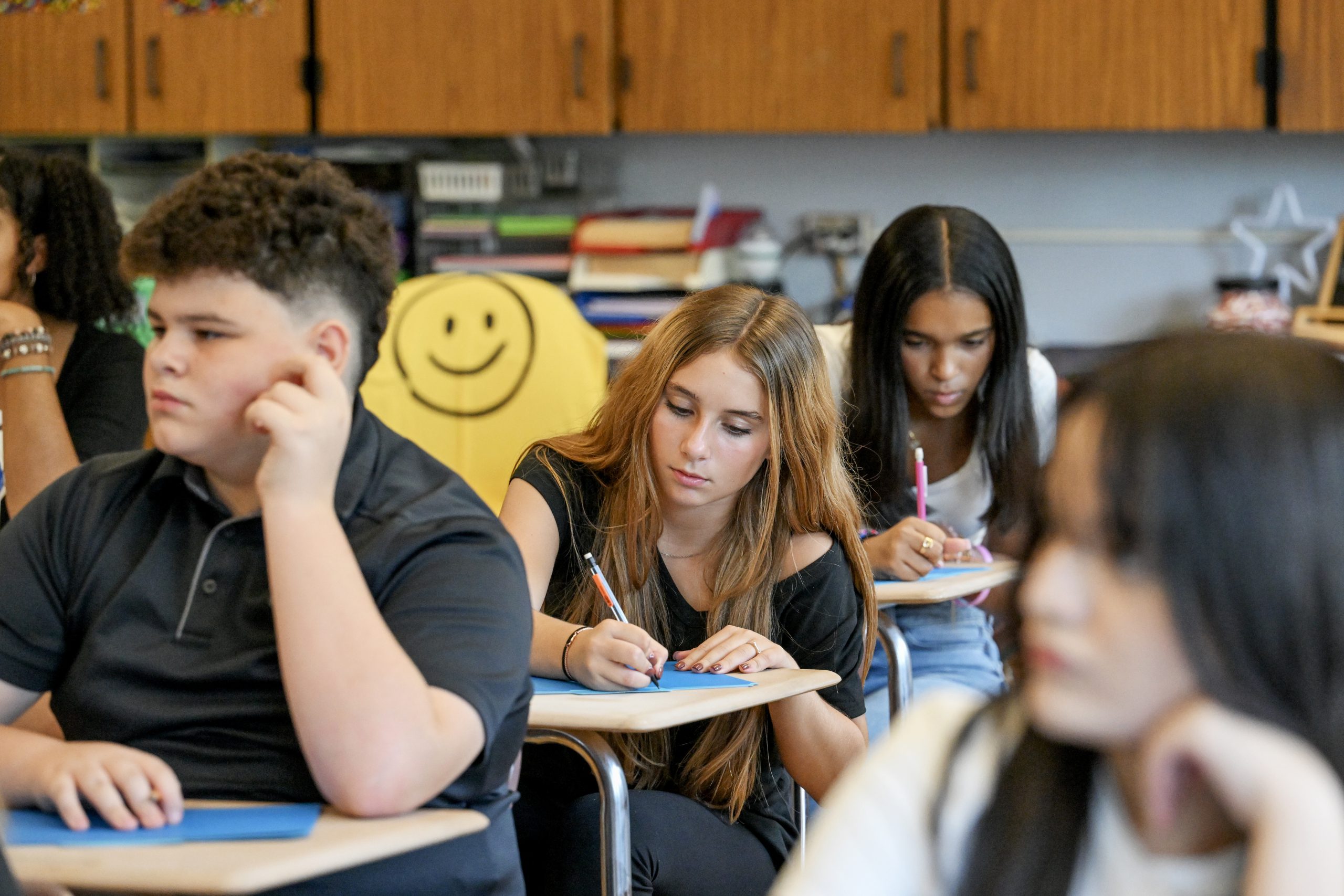 Junior high school students write at their desks in a classroom.