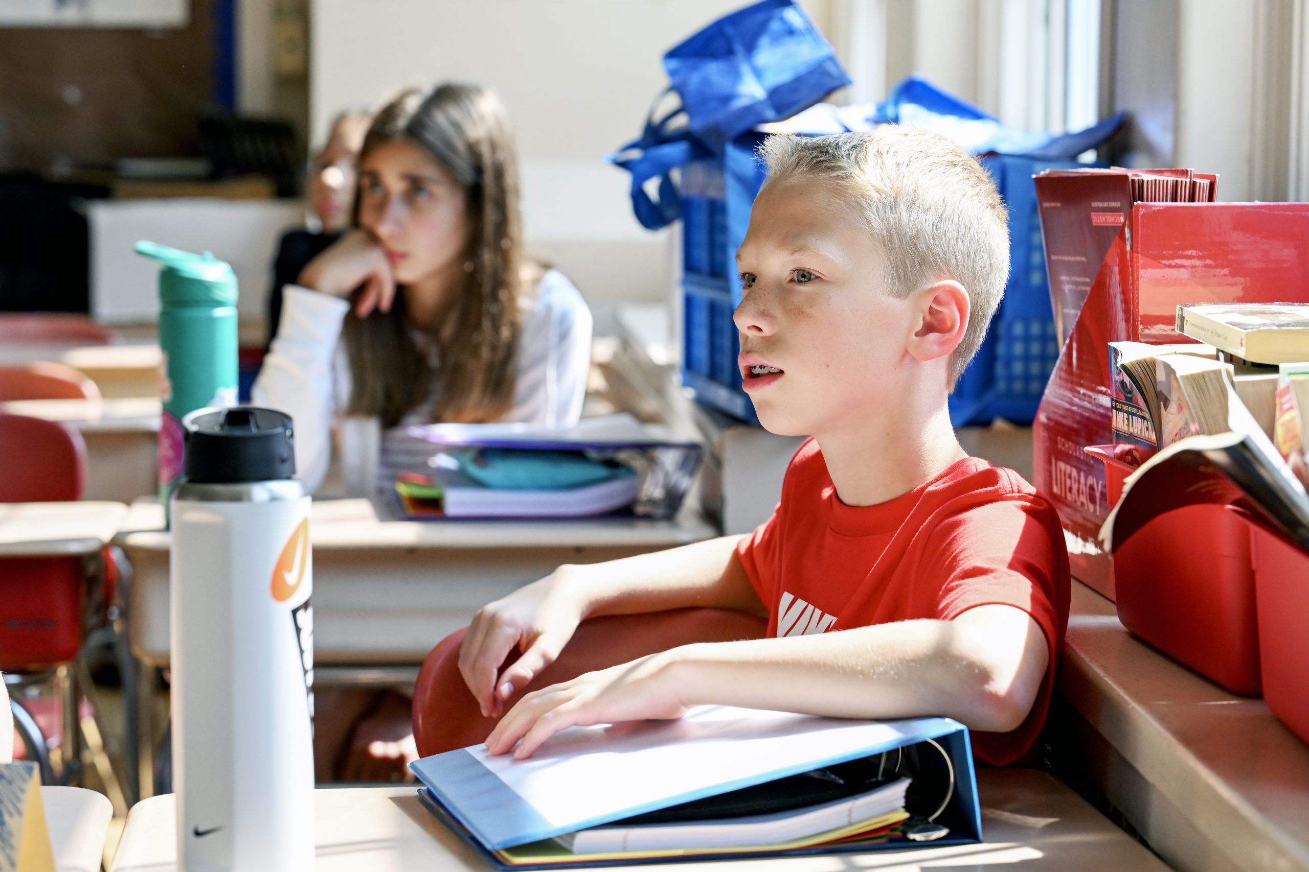 Young student sits at his desk in a classroom and listens intently