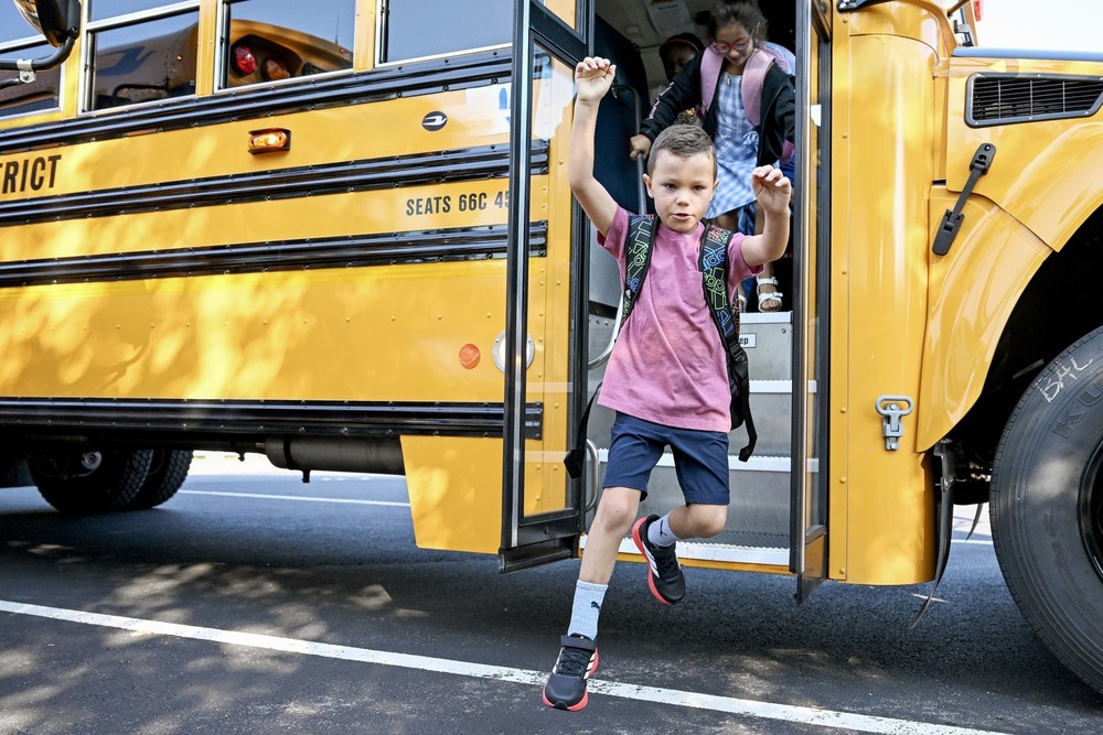 A young student jumps off the school bus with his arms overhead