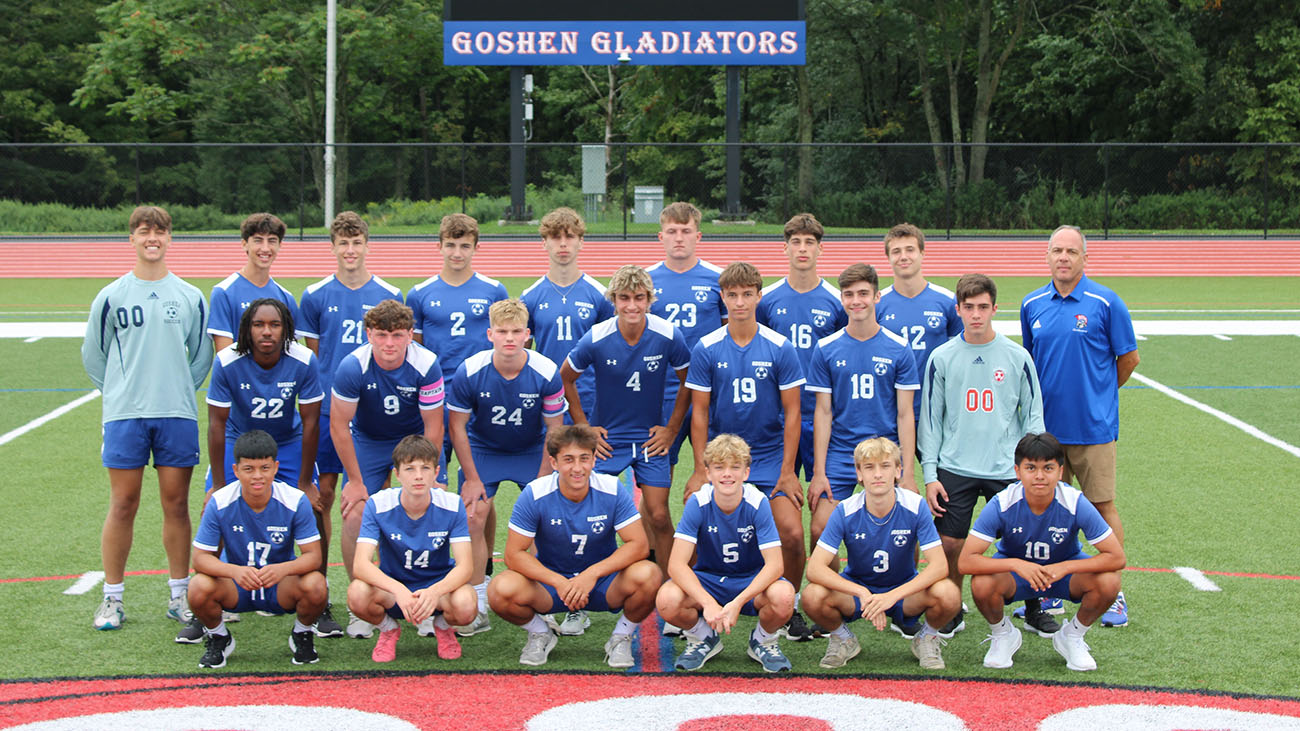 Boys soccer teams pose on the turf field in their blue soccer uniforms