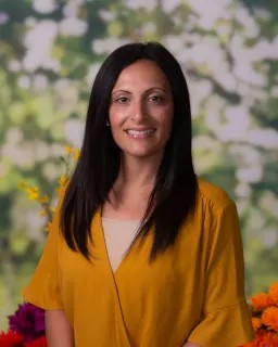 Adult with long dark hair smiling wearing a mustard colored shirt