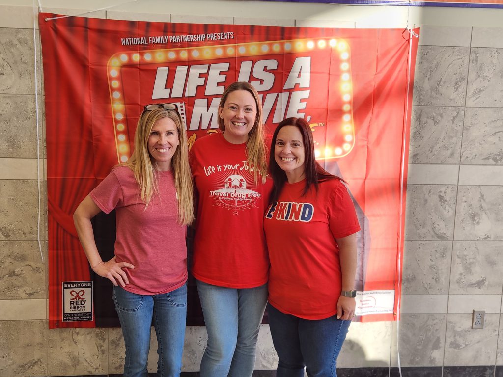 Goshen staff pose in front of a banner at Red Ribbon Week. 