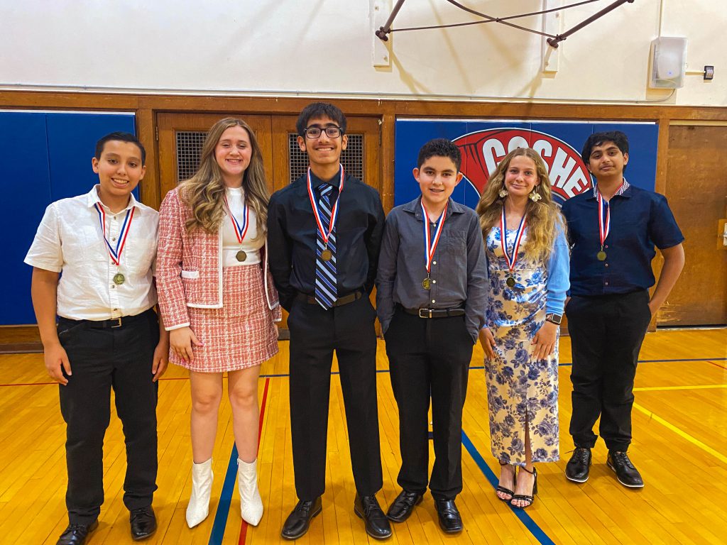 Six students stand next to each other all wearing medals. 