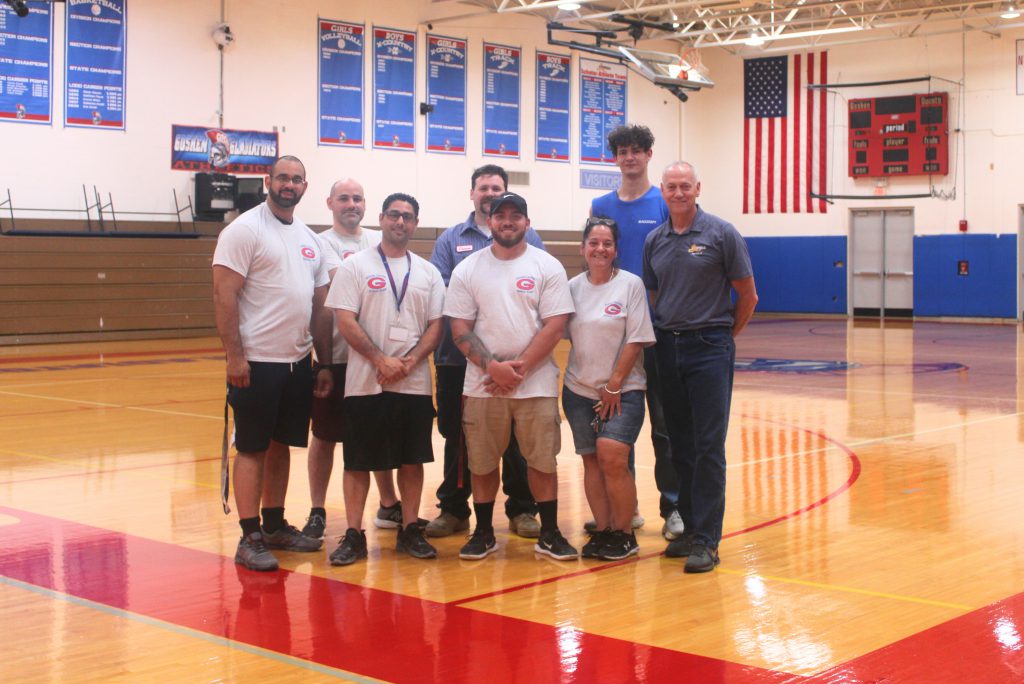 Goshen custodial staff stand for a picture on the new gym floor with athletic director George St. Lawrence. 
From left to right back row: Victor Reyes, Derrick Diaz, Connor Noonan, Matt Catrel. From left to right front row: Paul Giusto, (GHS Head Custodian) Derrick Cooper, Maria Cooley, George St. Lawrence (AD). Not pictured: Sean Boyle. 