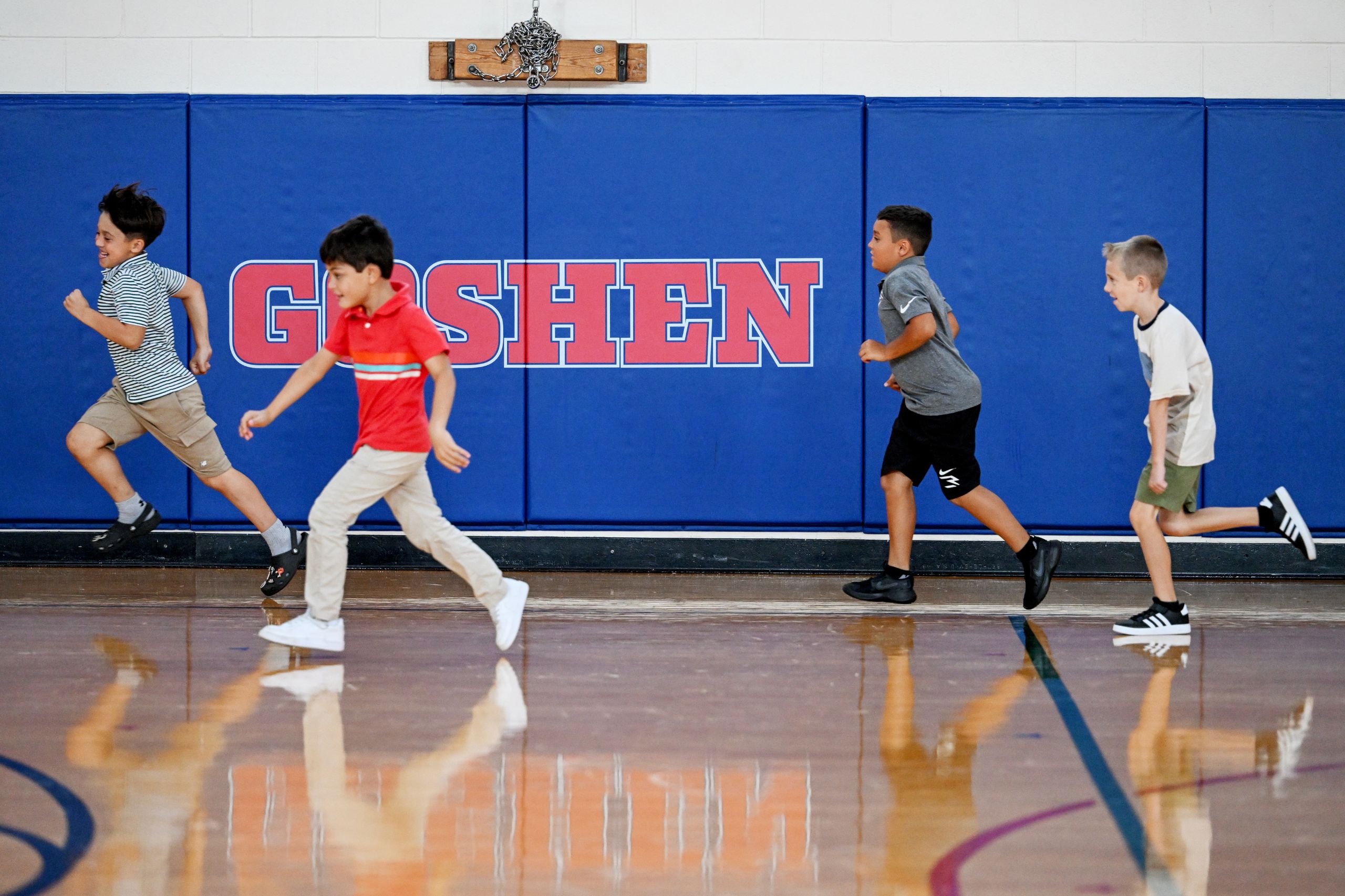 Students running in the gym with the word "Goshen" on the wall.