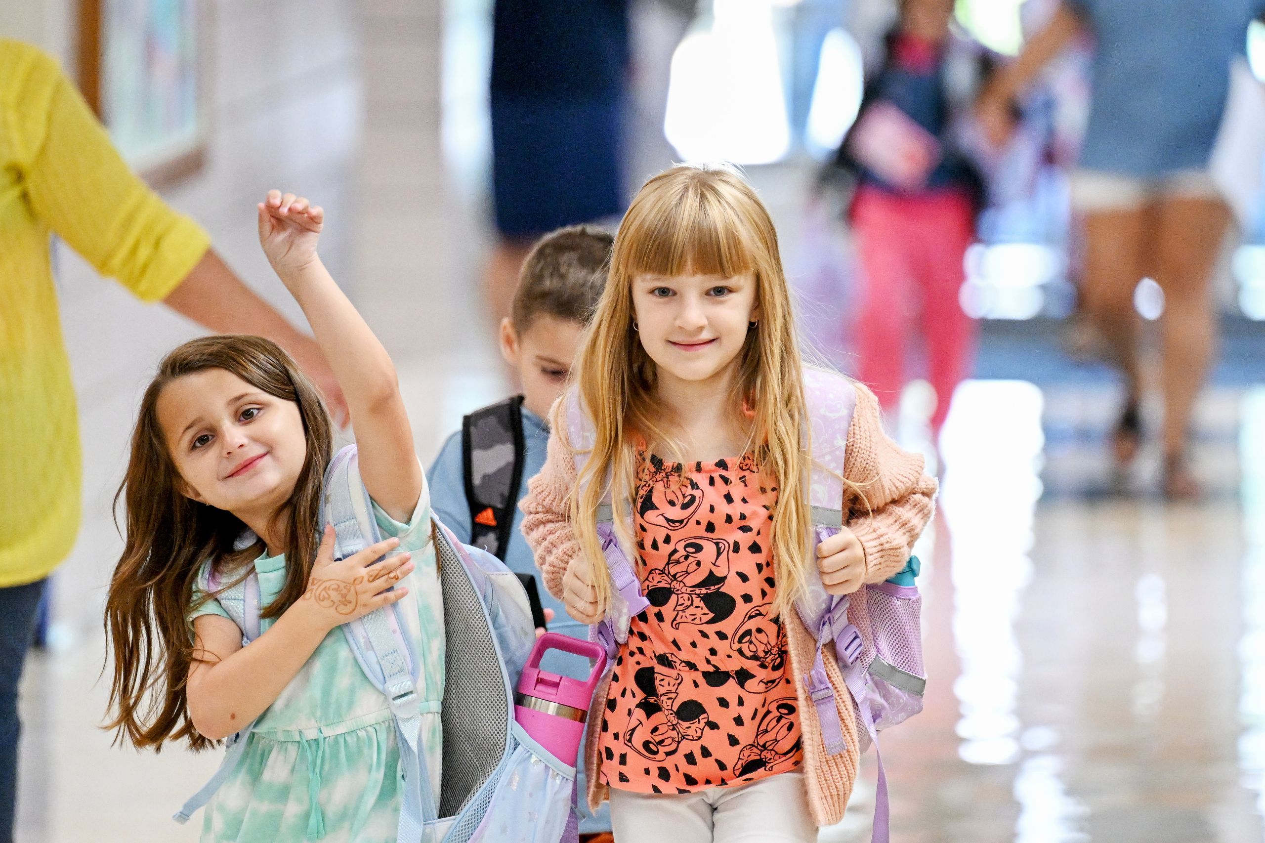 Three children walk to class on the first day of school in Scotchtown Avenue Elementary. The students are smiling and have backpacks in the hallway. 