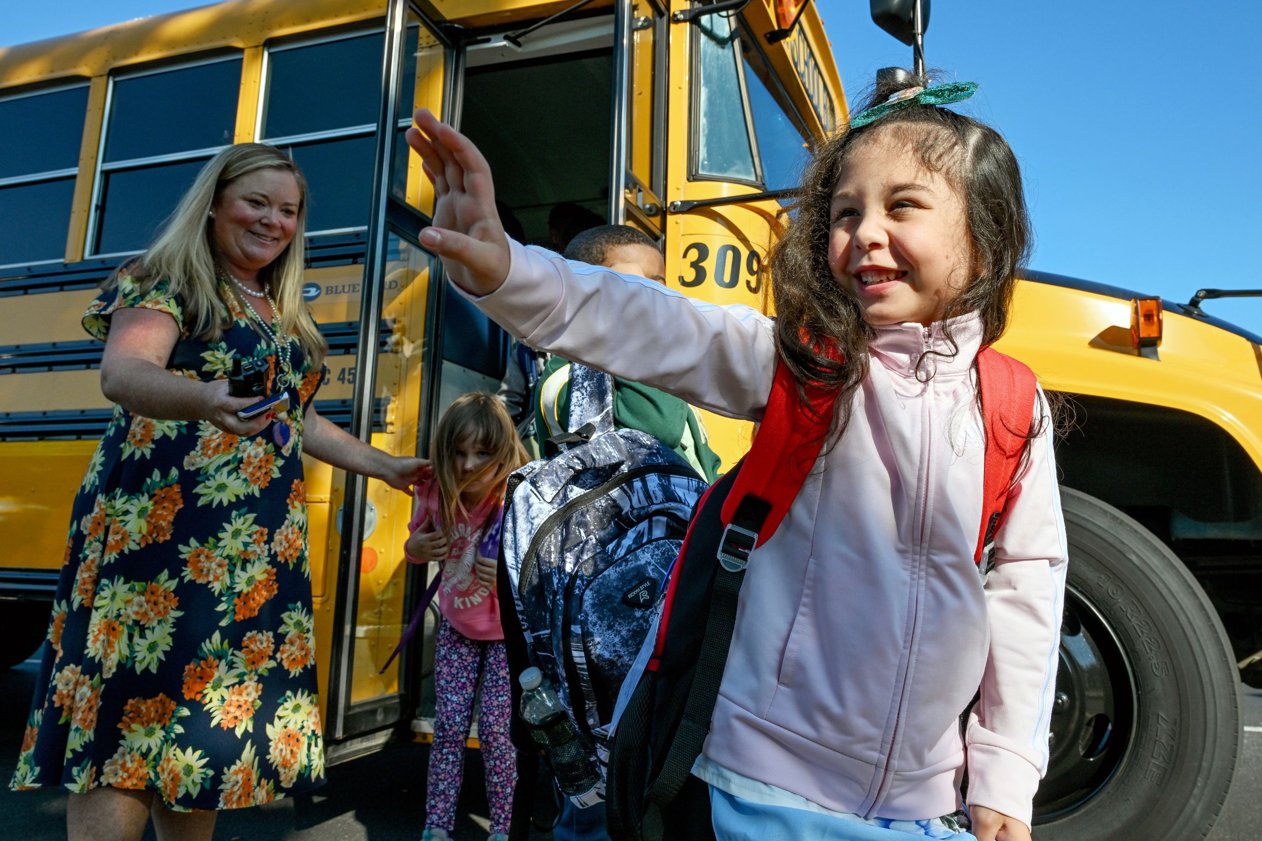 A student waves and smiles after getting off the bus. More students are getting off behind on their way to the first day of school. 