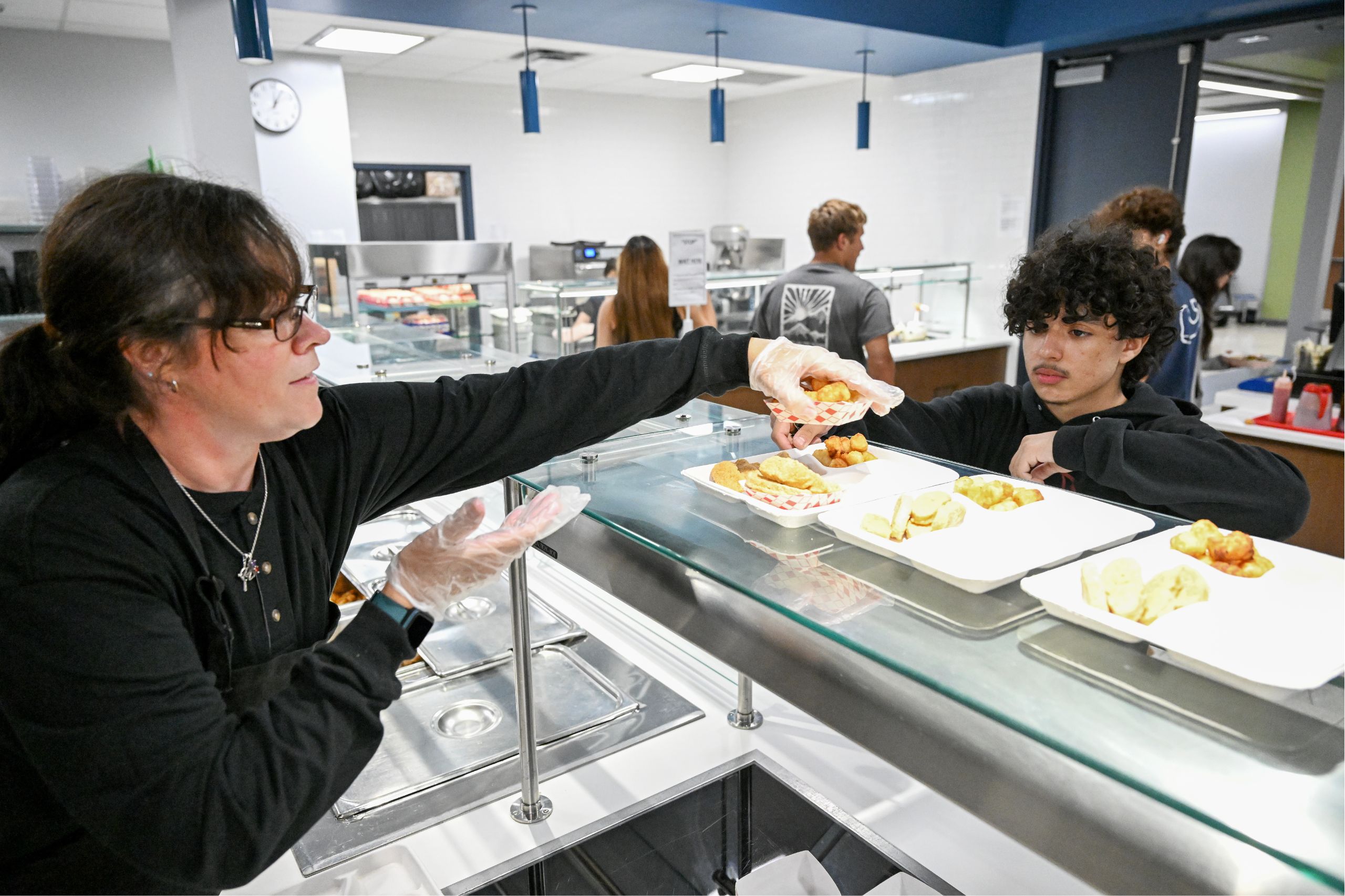 A student gets lunch in Goshen High School. A server is reaching over the glass at the counter to put food in the student's tray.