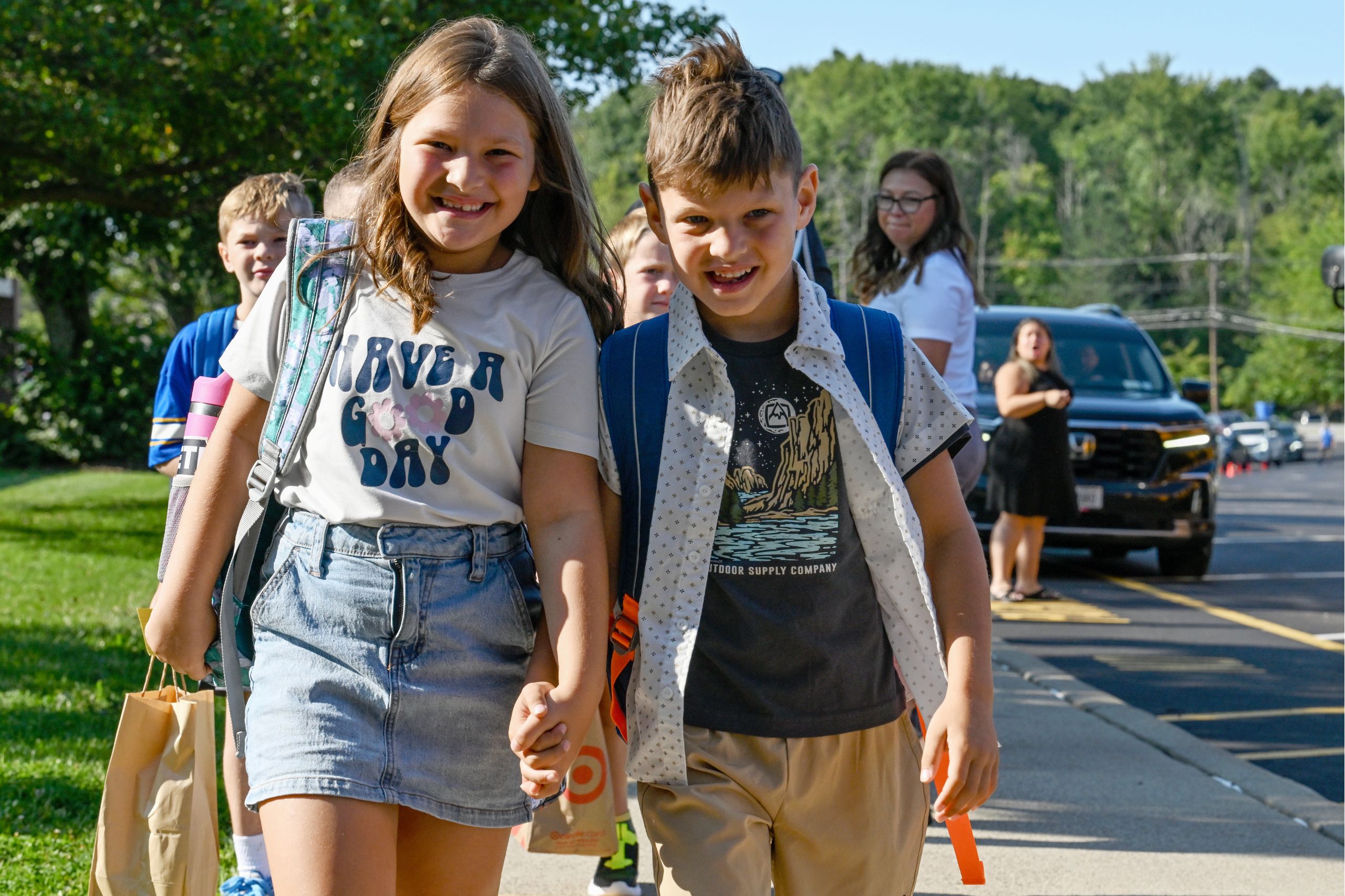 Two students walk into class together, one has an arm around the back of the other. 