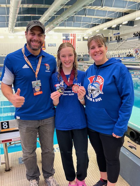 Kaylee Croughan holds a medal and poses with coaches Dr. Voloshin and Janet Albanese at the NYSPHAA swimming and diving championship. 