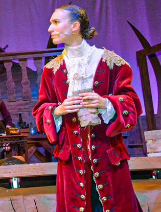 Jillian Kyrou on stage in a long red coat, in character as Doctor Livesey in Treasure Island.