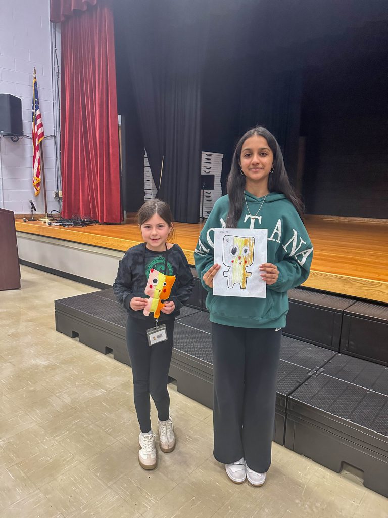 A Goshen High School student and Goshen Intermediate Student pose together. The high school student holds the drawing, and the intermediate student holds the sewn monster they collaborated on. 