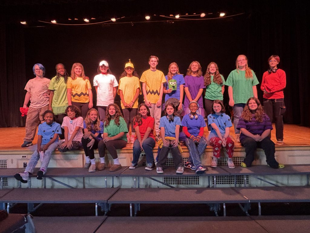 Students in costume on stage for the cast photo. Each student is in costume and is smiling for the camera. 