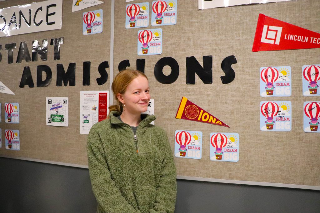 A student stands near her name under an "Iona" banner on the wall at the instant admissions board in the hallway at Goshen High School. 