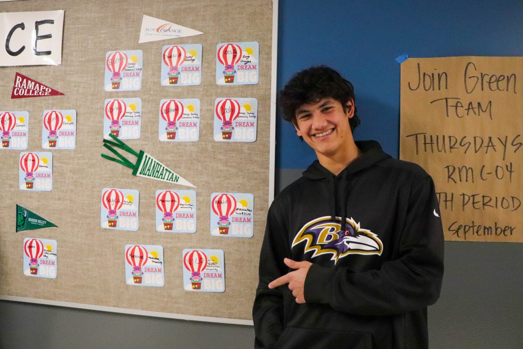 A student stands near his name under an "Manhattan University" banner on the wall at the instant admissions board in the hallway at Goshen High School. 