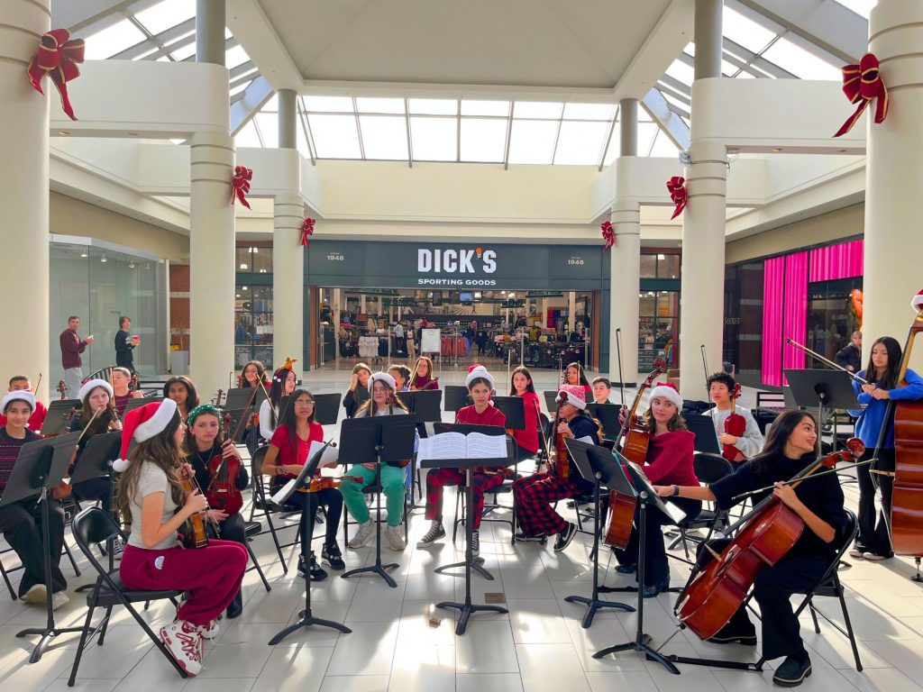 Group photo of the C.J. Hooker students performing at the Galleria Mall in Middletown. The students are seated and in position to perform with their instruments. 