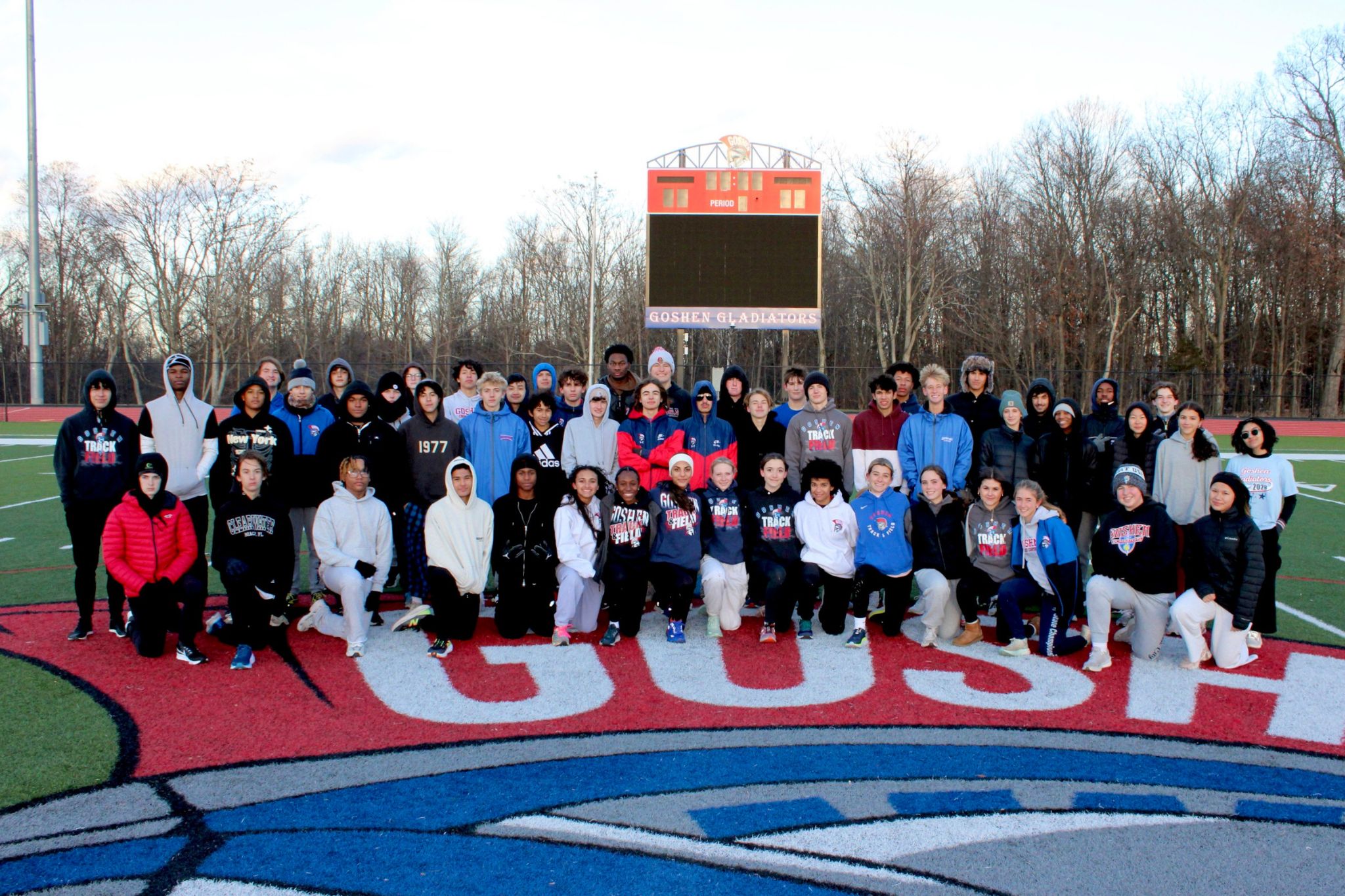 Goshen's Varsity Winter Track team. Everyone is standing together on the football field with the Goshen logo below them. 