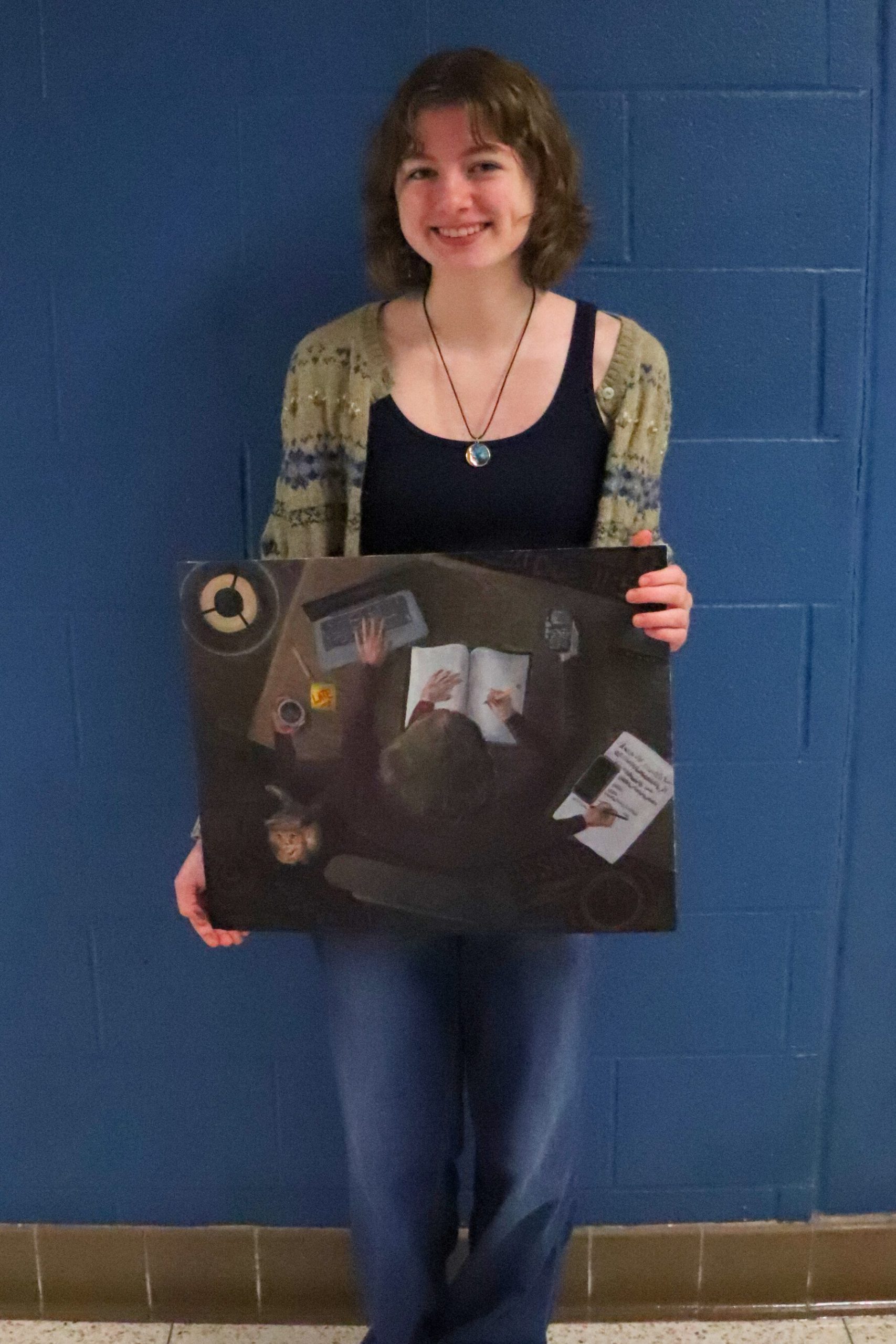 Ava Carroll stands with her painting titled "Stressing." The painting is a view from above a person at a desk with a child in her lap. 