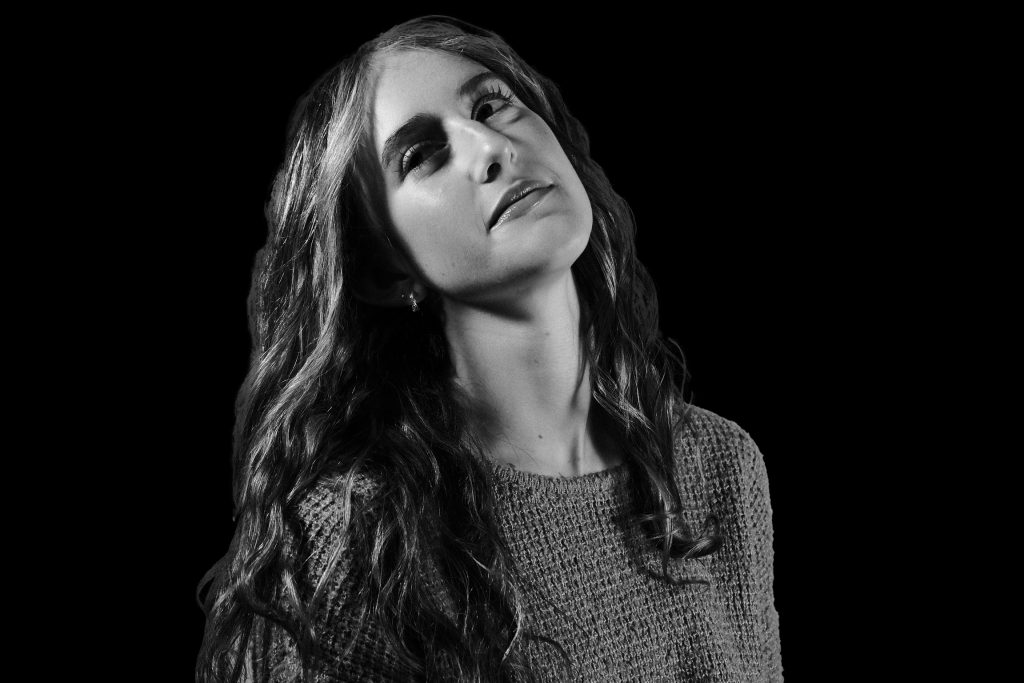 A black and white photo of a girl looking over her right shoulder away from the camera. Her head is slightly tilted backward. 