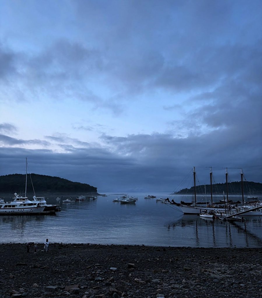 Boats on a late, photo is taken from the beach. It is getting dark and there is blue sky to the left of some clouds. 