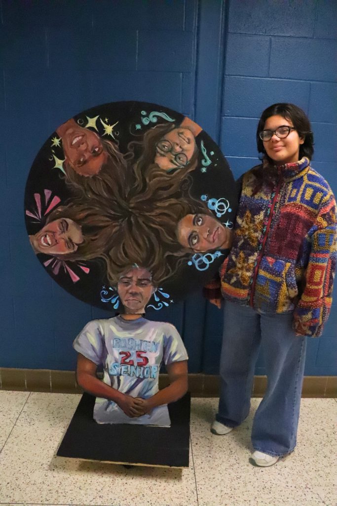 Katie Palau stands next to her wooden sculpture titled Mood Wheel.