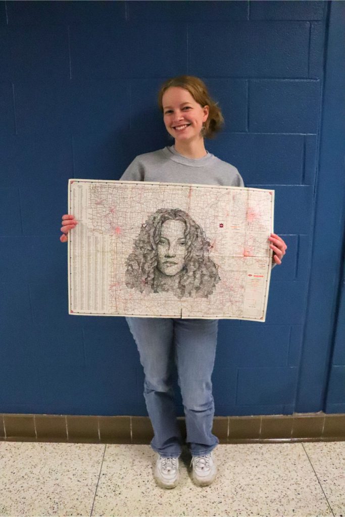 Goshen student Lefa Brown smiles and holds her drawing of Sheryl Crow over a map of Missouri. 