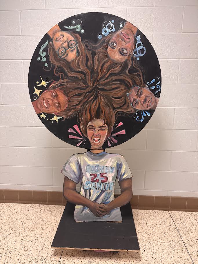 A wooden sculpture with five faces of a girl that depict various moods. The faces are on a wheel and can be spun to line up with a neck and upper body below. 