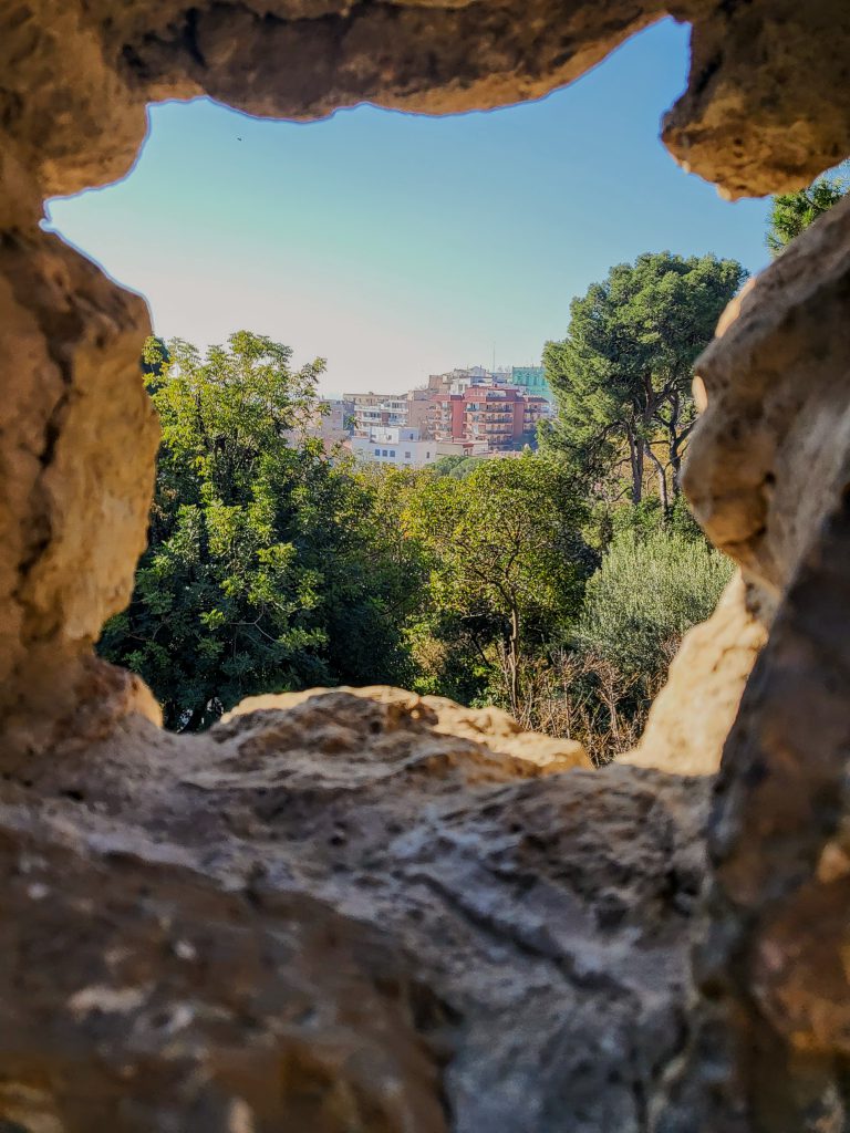 A photo taken looking out at buildings from the perspective of inside of a narrow cave. 