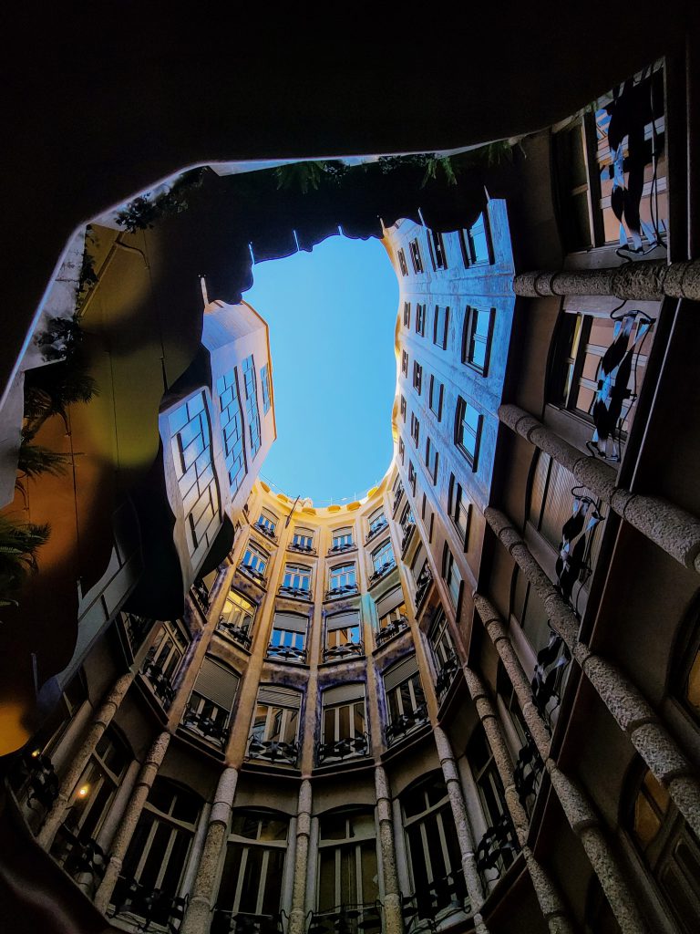 A photo taken looking up from below A spiraling building. There are windows on the building and it is a sunny day. 