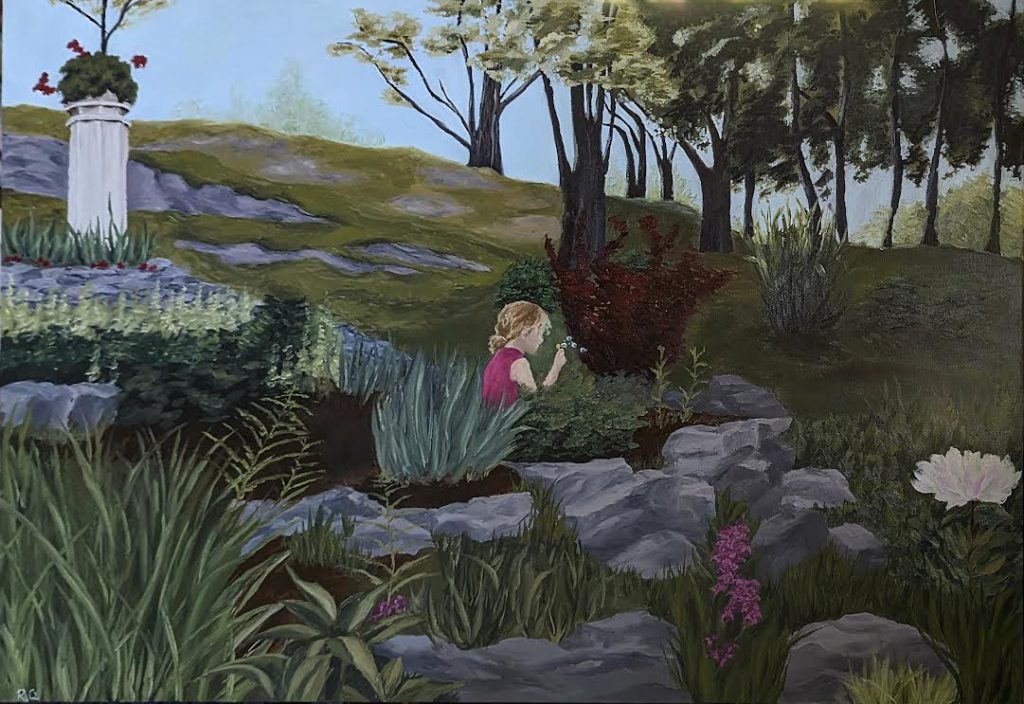 A girl sits in plants looking at something she picked up. The setting is outside in nature with trees and plants surrounding the girl who is looking away from the viewer. 