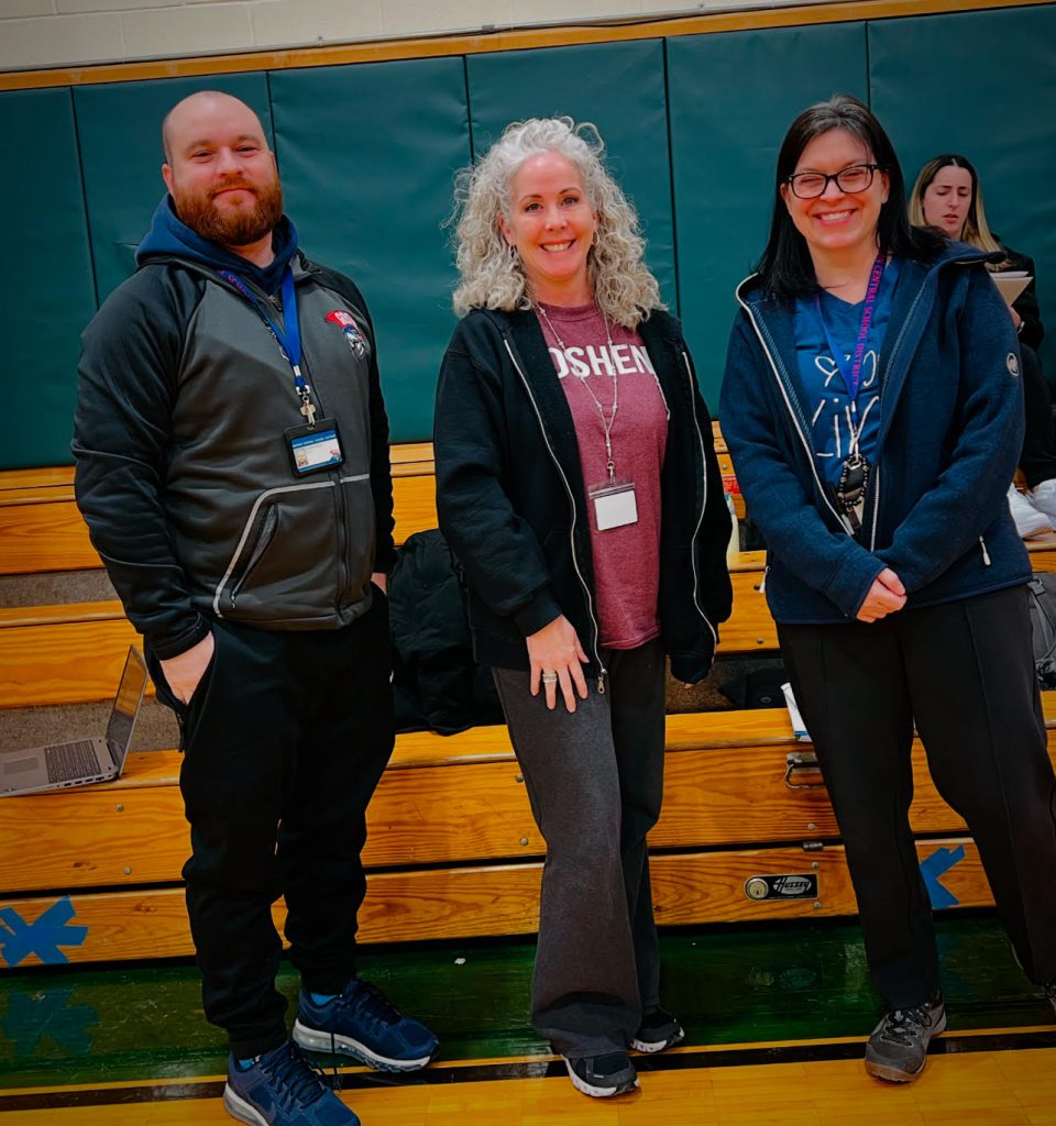 Charles Doyle, Heather Hendershot and Kristen Kurpick stand next to each other in a gym. They are all smiling and wearing Goshen athletic attire. 