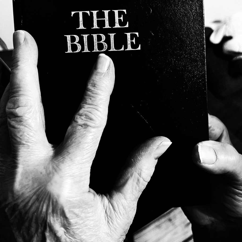 A hand is on a bible. The photo is black and white.