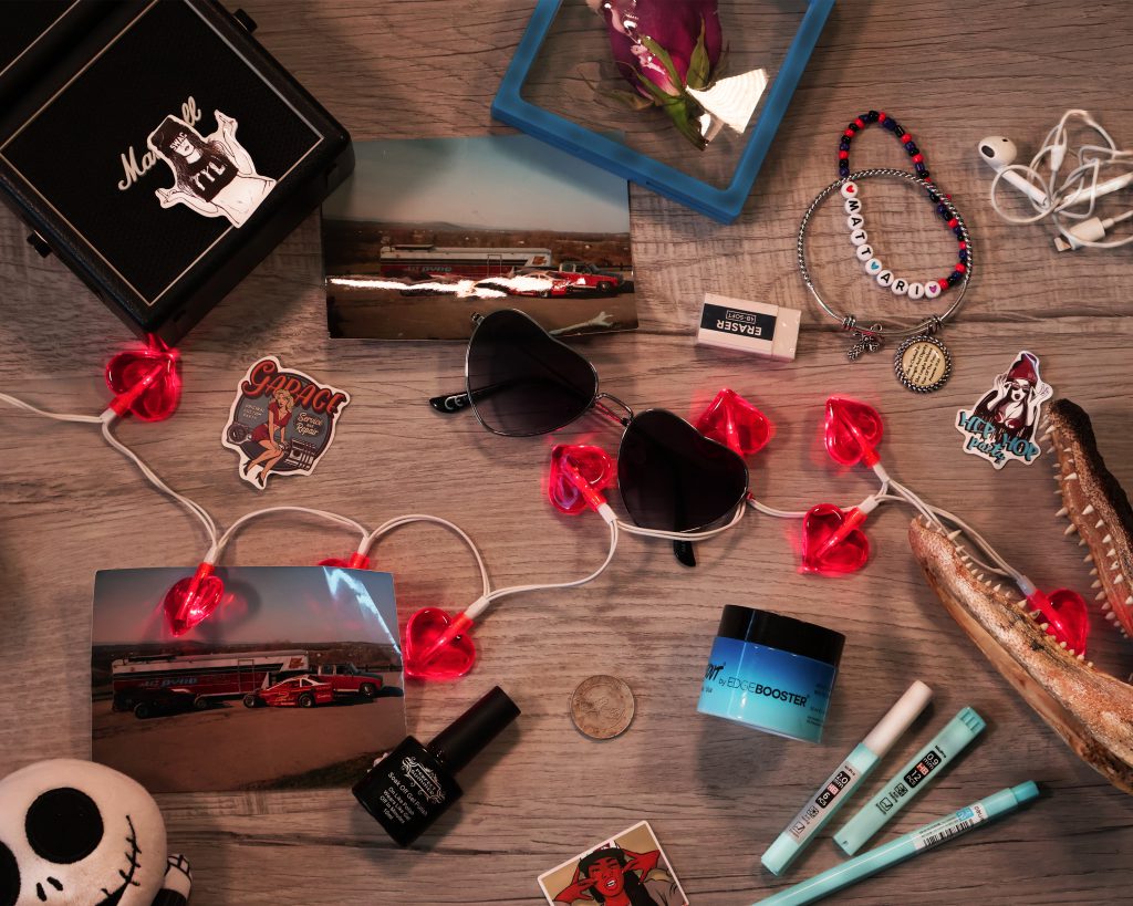 Items are scattered on a table in full color. The items are heart shaped glasses, heart lights, photos, stickers, bracelets, and others. 