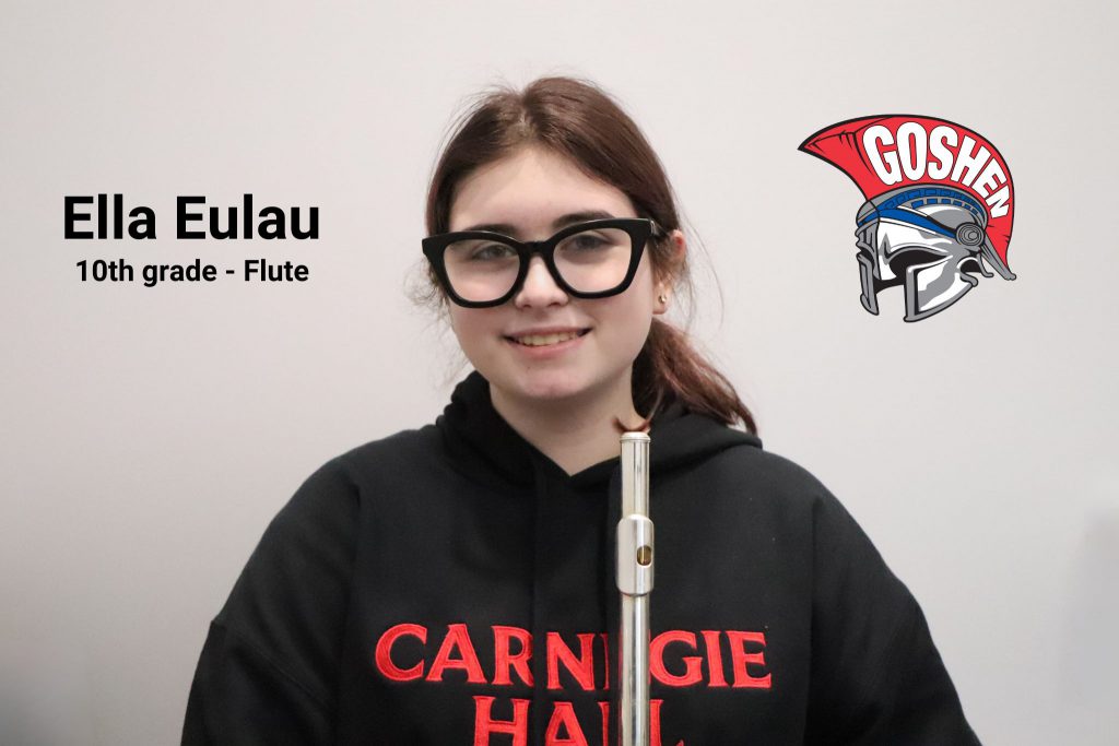 Ella Eulau stands with her flute in a Carnegie Hall sweater. She smiles for the camera. The photo has her name along with 10th grade flute written on it and the Goshen Gladiators' helmet logo. 