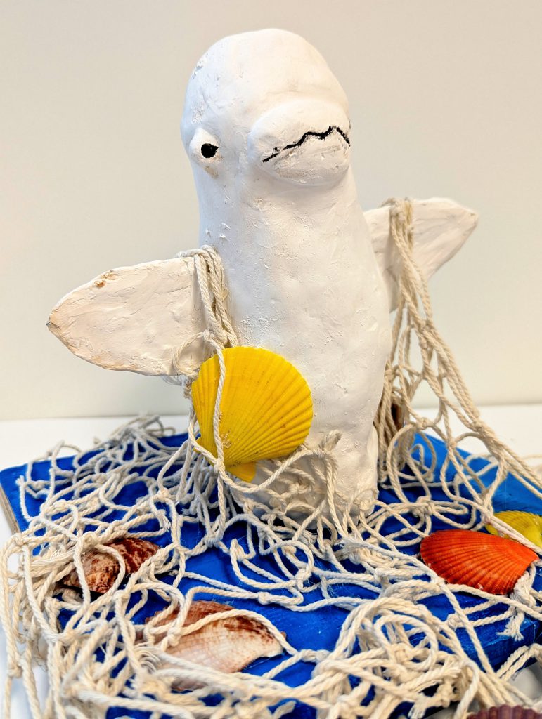 An ocean animal is reaching up through a net with shells on a blue ground. 