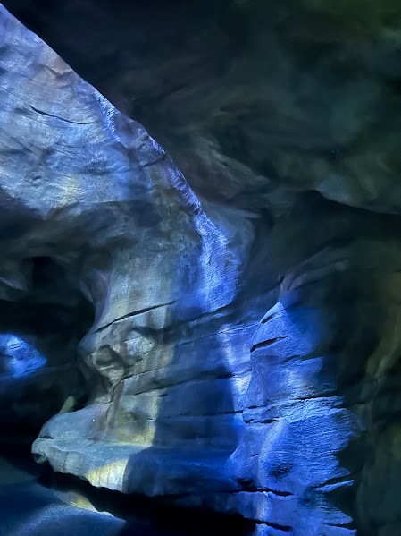 A wall made of rocks has a blue glow on it with water reflecting up onto the bending rock structure out of frame of the photo. 