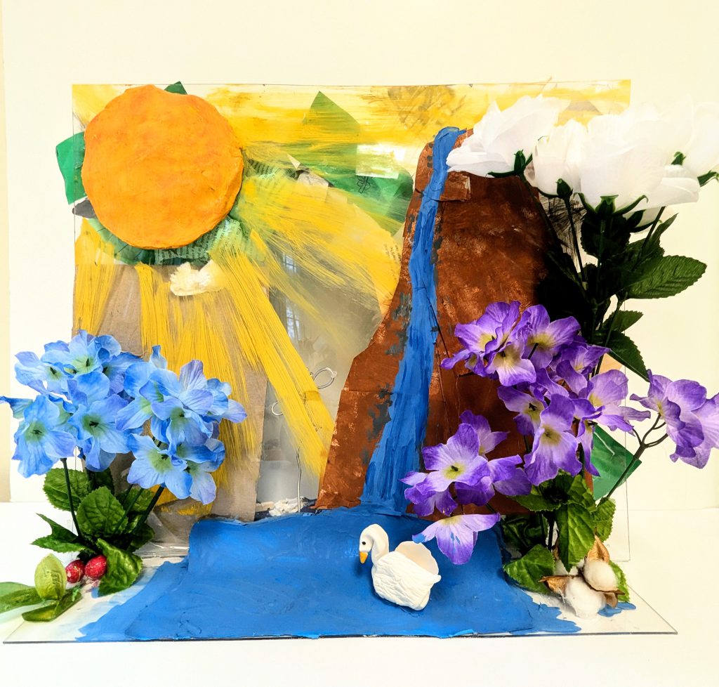 A large waterfall with a sun and flowers around a water area with a swan swimming around all made of different fabrics, clay, and painted-on structures. 